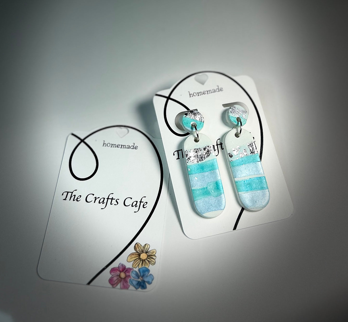 Unique handmade polymer clay earrings in turquoise and white with silver foil, scalloped edges, on The Crafts Cafe display card