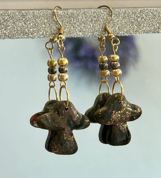 Pair of earrings with dark stone-like beads and gold accents on a reflective surface.