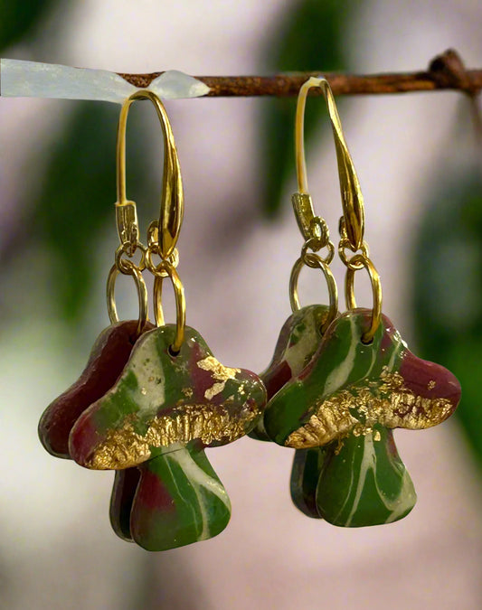 Pair of earrings with gold accents and marbled green and red design hanging on a branch.